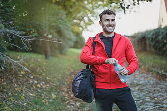 Smiling Man in Red Jacket Drinking Water in Park