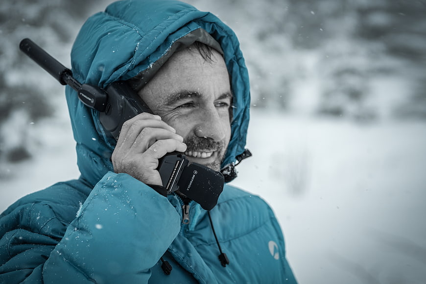 Man in Blue Jacket Talking on Radio in Snow