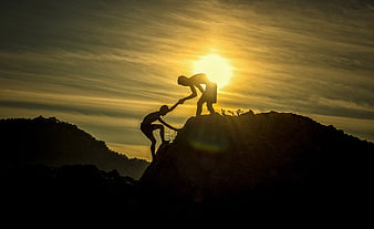 Silhouette of Two Hikers Helping Each Other Climb a Mountain at Sunset
