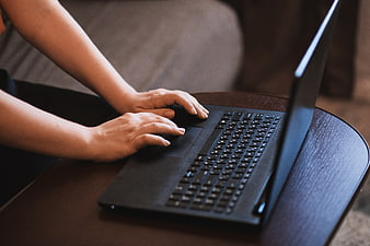 Close-up of hands typing on a black laptop keyboard