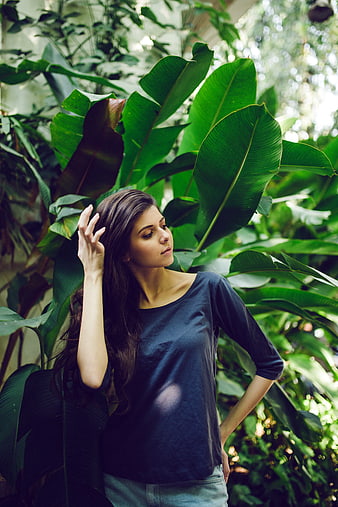 Woman with long hair posing among lush tropical green leaves