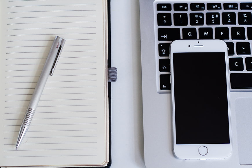 Flat lay of notebook, pen, smartphone, and laptop keyboard