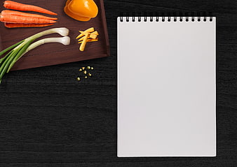 Fresh vegetables on wooden tray with blank notebook on black table
