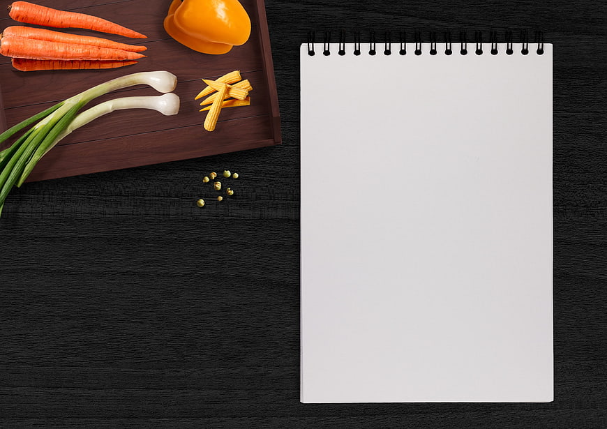 Fresh vegetables on wooden tray with blank notebook on black table