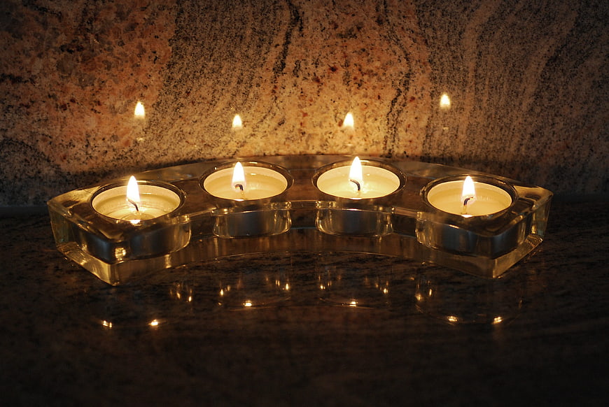 Four lit tealights in glass holder on granite