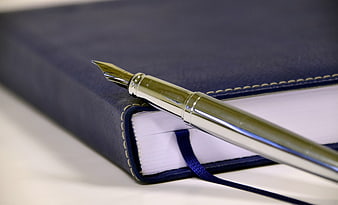 Gold fountain pen resting on a navy blue leather notebook