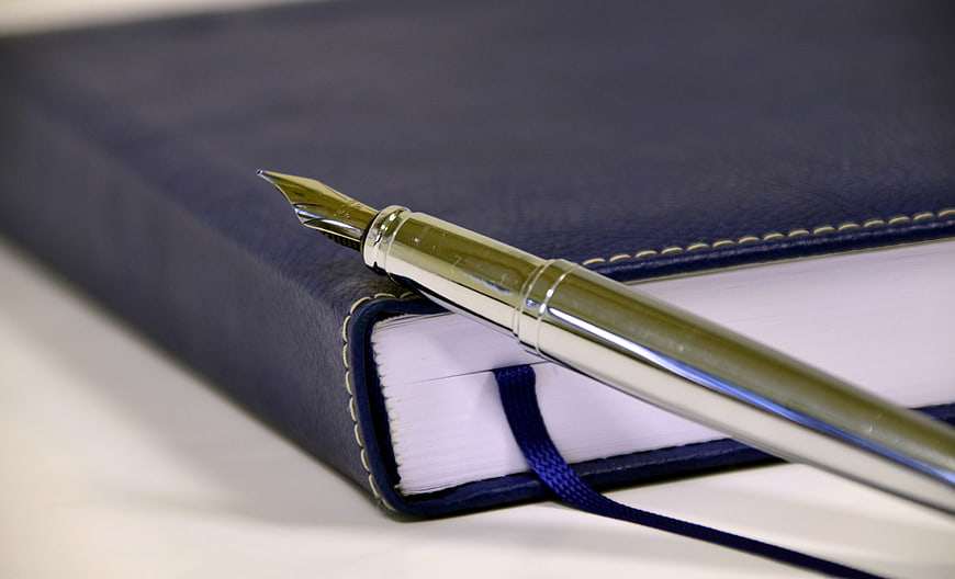 Gold fountain pen resting on a navy blue leather notebook