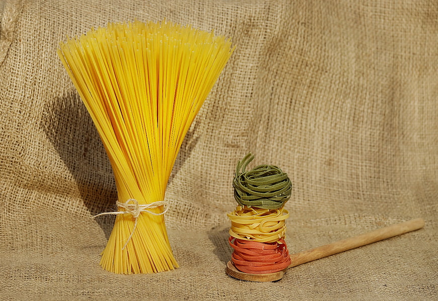 Raw spaghetti and colorful pasta nests on rustic burlap background