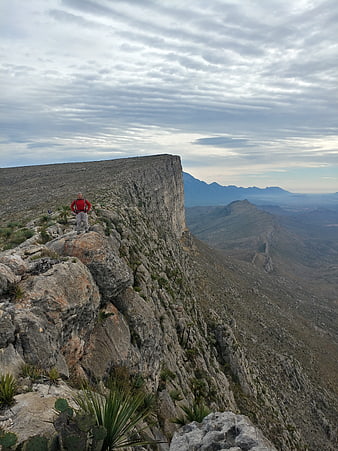 Hiker standing on rocky mountain cliff edge with vast landscape