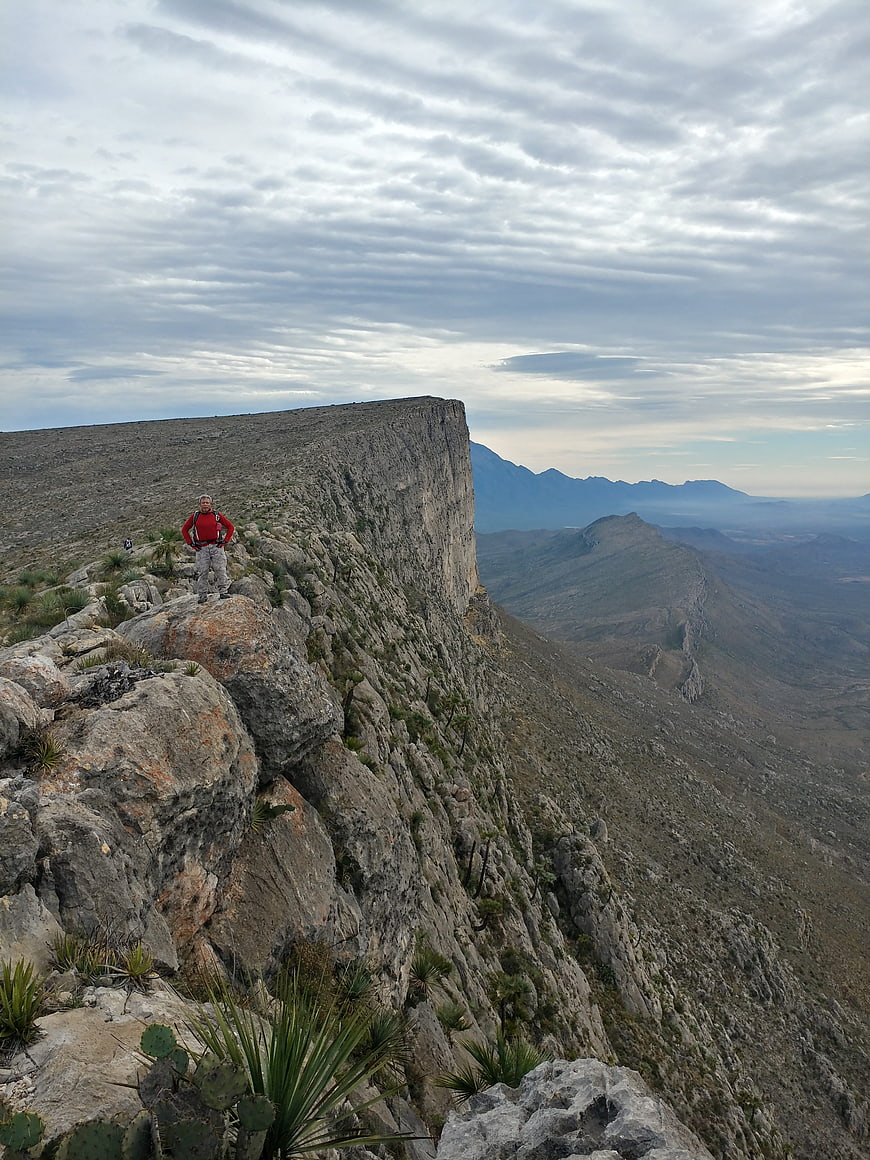 Hiker standing on rocky mountain cliff edge with vast landscape