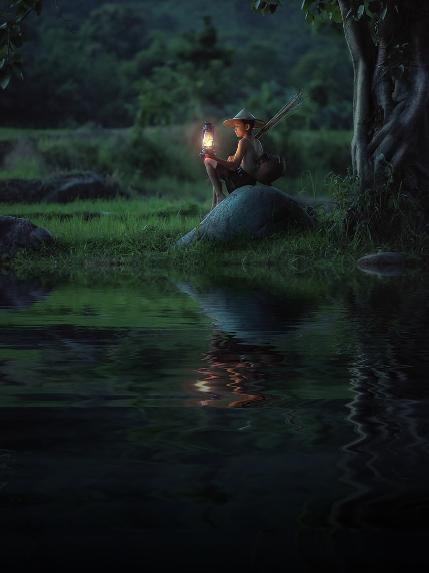 Boy with Lantern Sitting by River at Night