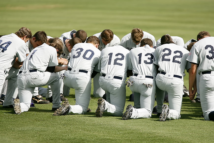 Baseball team kneeling in prayer on green grass field
