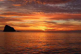 Dramatic Orange Sunset Over Calm Ocean with Silhouetted Rock