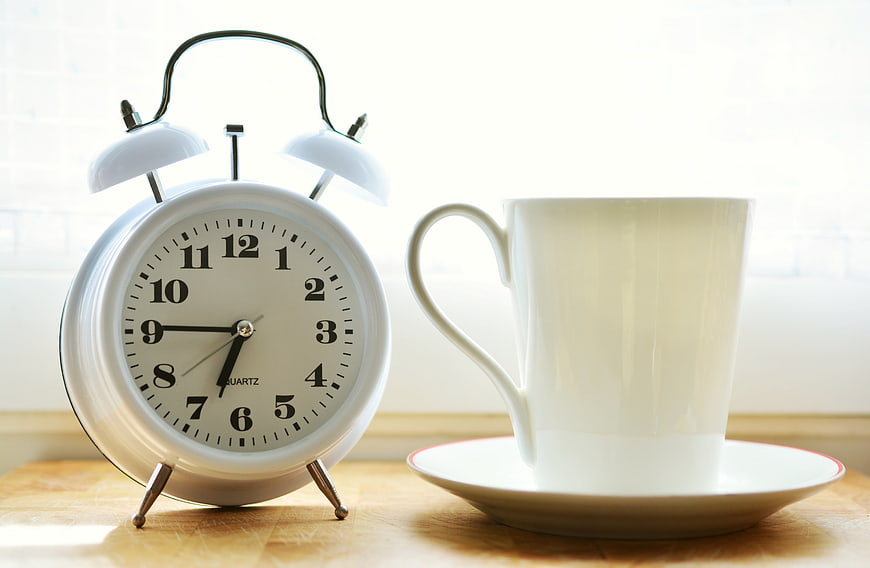 White Alarm Clock and Coffee Cup on Wooden Table