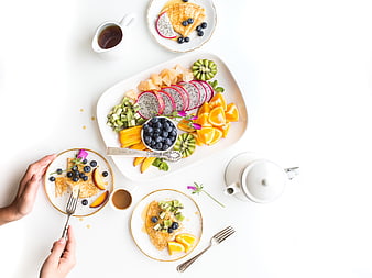 Healthy breakfast spread with pancakes, fresh fruit platter, and tea on white table