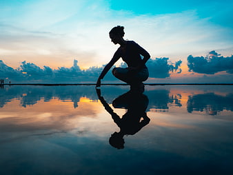 Silhouette of woman touching water reflection at sunset