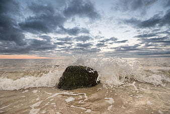 Dramatic ocean wave crashing against mossy rock at sunset