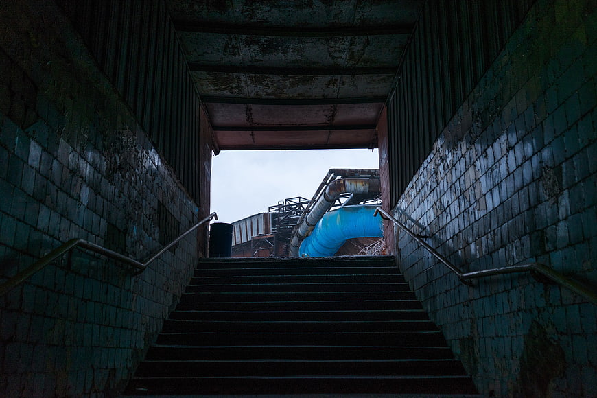 Dark industrial stairs leading to blue pipe structure