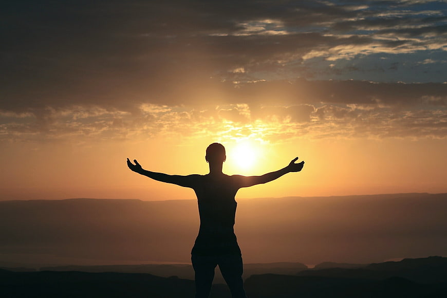 Silhouette of woman with arms raised at sunrise