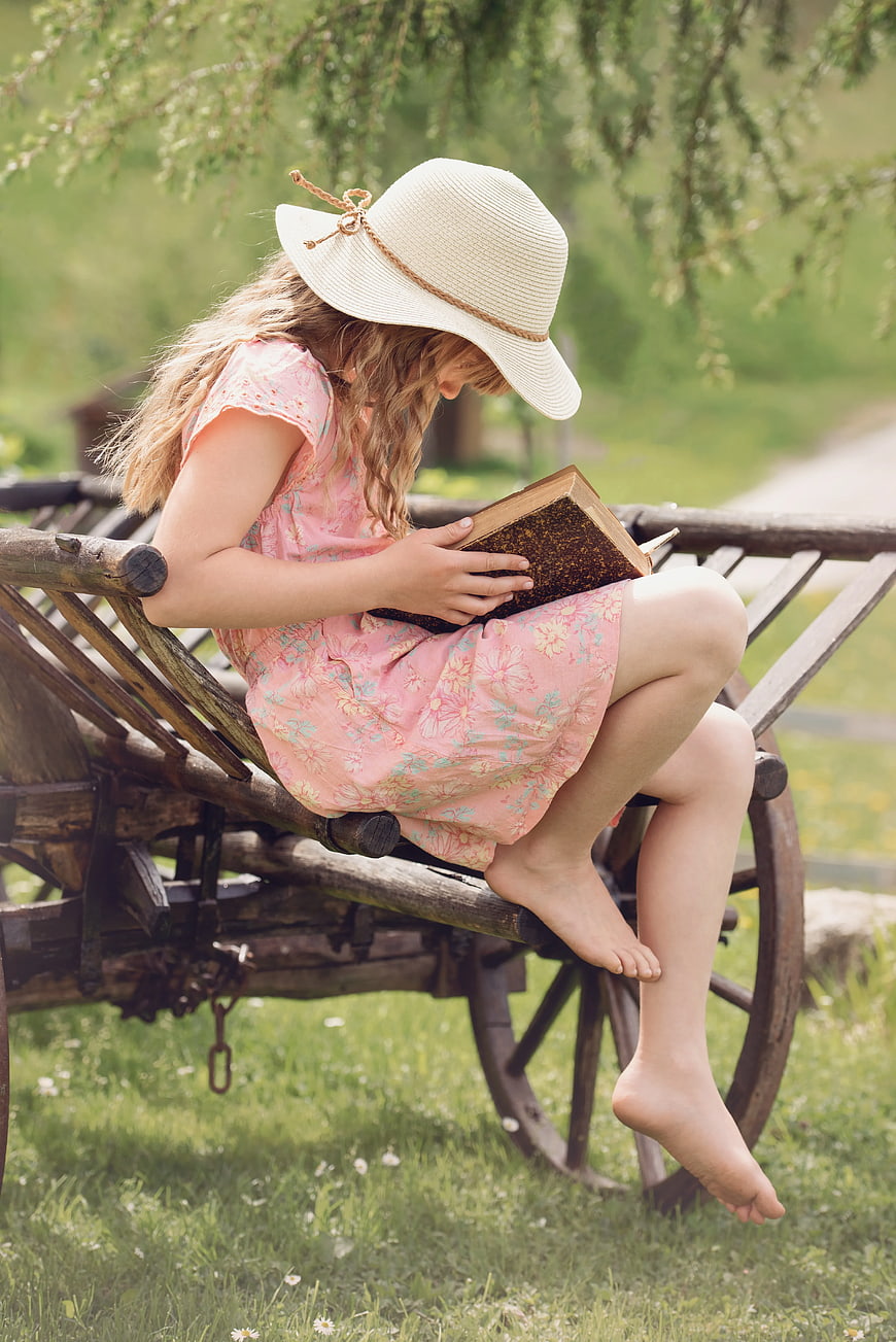 Young Girl Reading Book on Vintage Wooden Cart