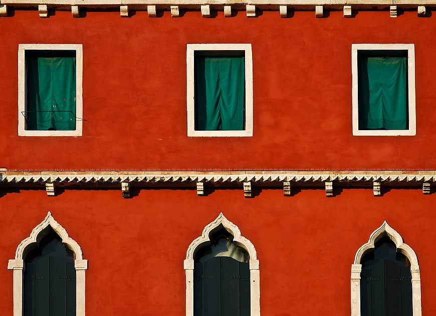 Red Venetian building facade with green curtains and arched windows