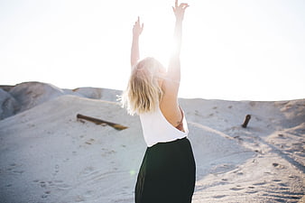 Woman with arms raised on sand dunes in sunlight