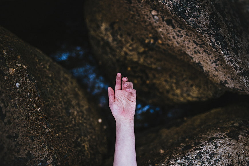 Hand reaching out from between dark rocks near water