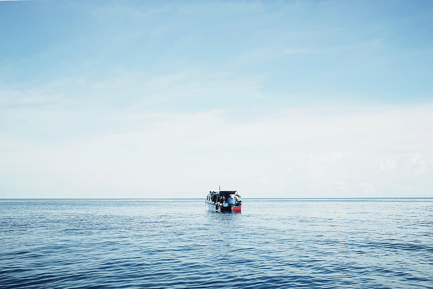 Small boat sailing on calm blue ocean horizon