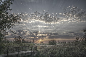 Dramatic sunset with sun rays over grassy landscape and bridge