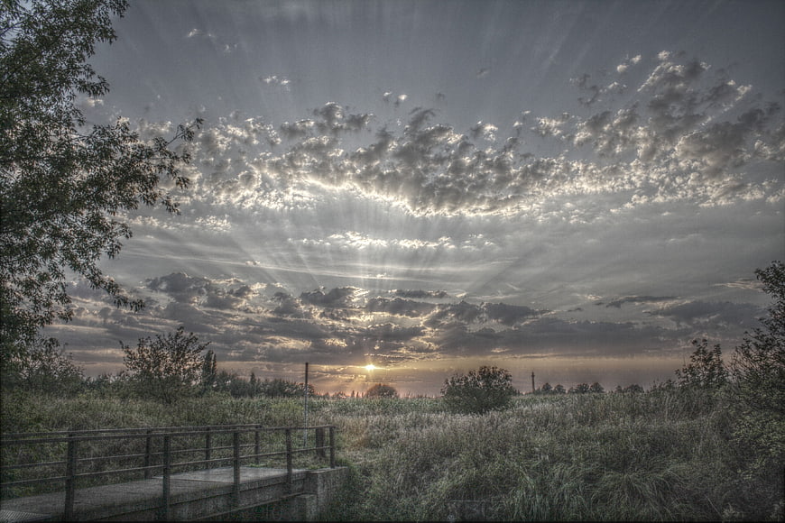 Dramatic sunset with sun rays over grassy landscape and bridge