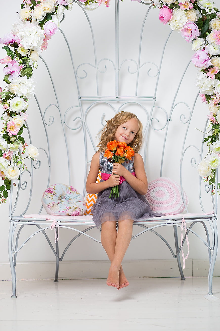 Cute little girl holding orange roses on floral bench