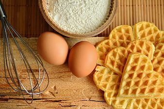 Heart-shaped waffles with eggs, flour, and whisk on rustic wood