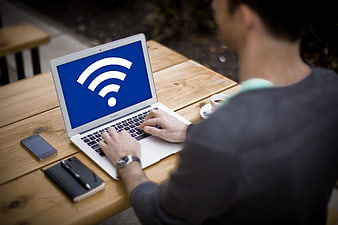 Man typing on laptop with Wi-Fi icon at outdoor wooden table