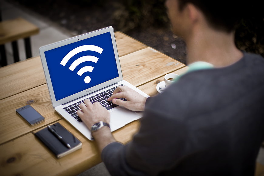 Man typing on laptop with Wi-Fi icon at outdoor wooden table
