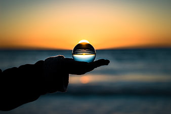 Hand Holding Crystal Ball at Sunset Over Ocean