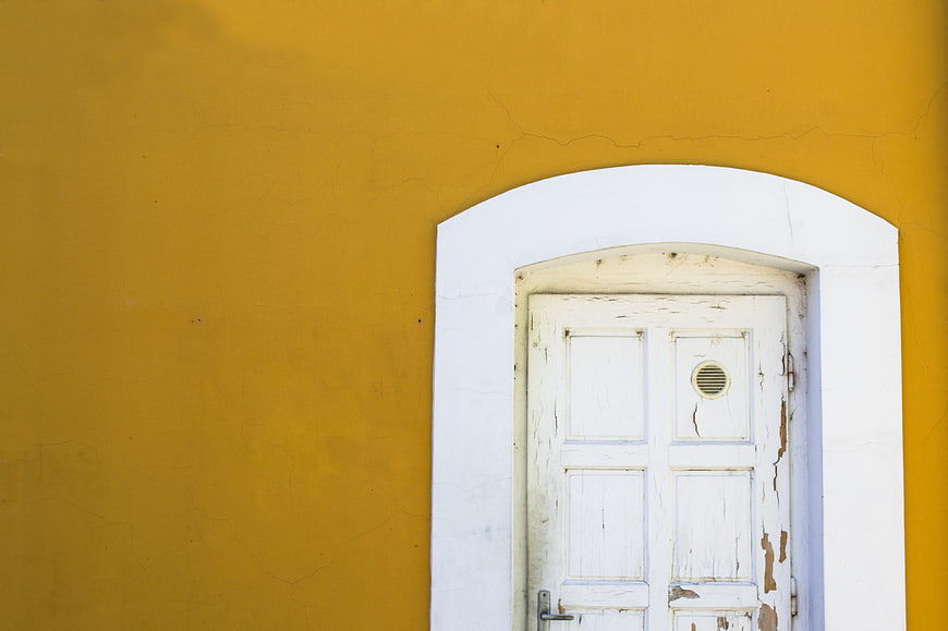 Weathered white wooden door in yellow wall with copyspace
