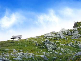 Lone Wooden Bench on Rocky Mountain Slope with Blue Sky