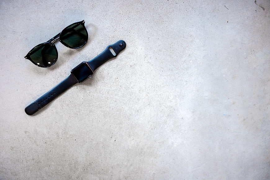 Black smartwatch and sunglasses on textured concrete background