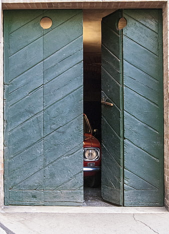 Vintage red car peeking through open green wooden garage doors