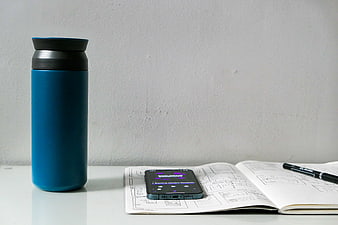 Blue Thermos, Smartphone, and Sketchbook on White Desk