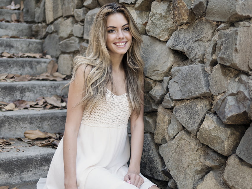 Smiling Young Woman in White Dress Sitting on Stone Steps