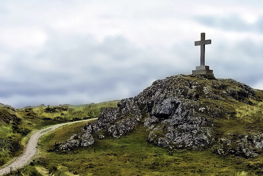 Stone cross on rocky hilltop with winding path