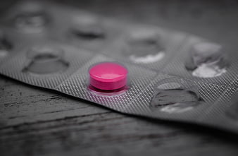 Single pink pill in blister pack on dark wood
