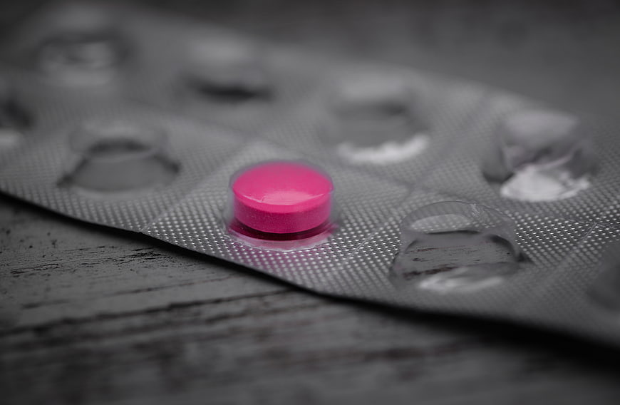 Single pink pill in blister pack on dark wood