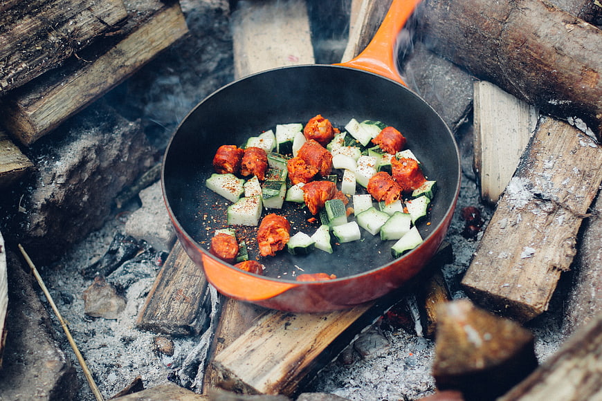 Camping cooking with sausage and vegetables in a pan over a fire