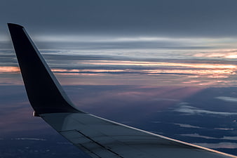 Airplane wing silhouette against a colorful sunset sky above clouds