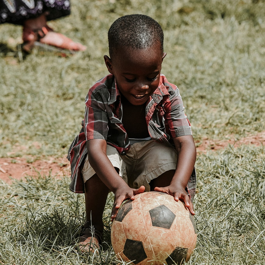 Happy African Child Playing with Soccer Ball on Grass