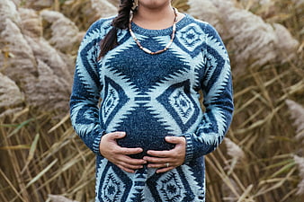 Pregnant woman in patterned sweater holding belly outdoors