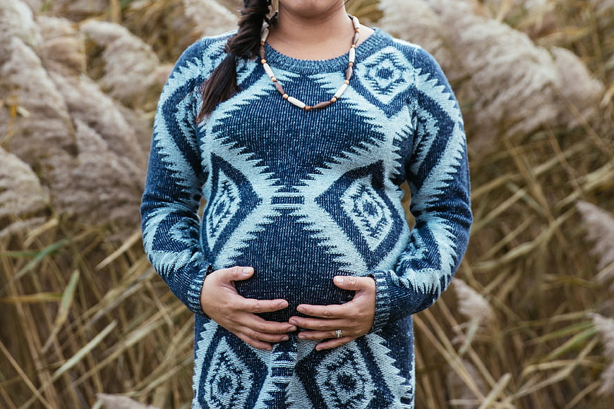 Pregnant woman in patterned sweater holding belly outdoors