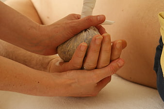 Close-up of hands performing herbal stamp massage on a client's back